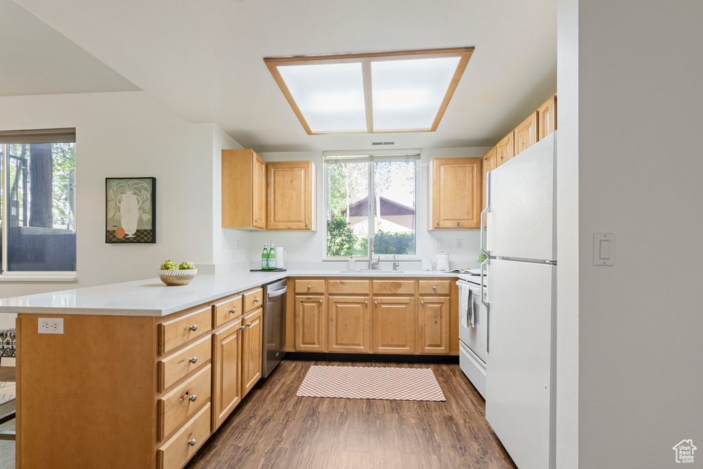 Kitchen featuring white appliances, a peninsula, dark wood-style floors, light countertops, and light brown cabinetry
