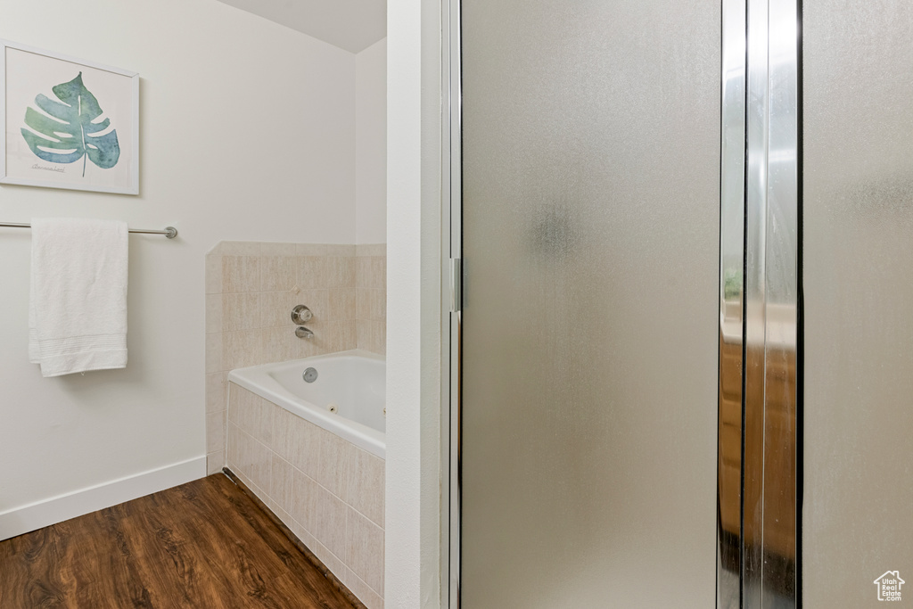 Bathroom featuring a stall shower, baseboards, a jetted tub, and wood finished floors