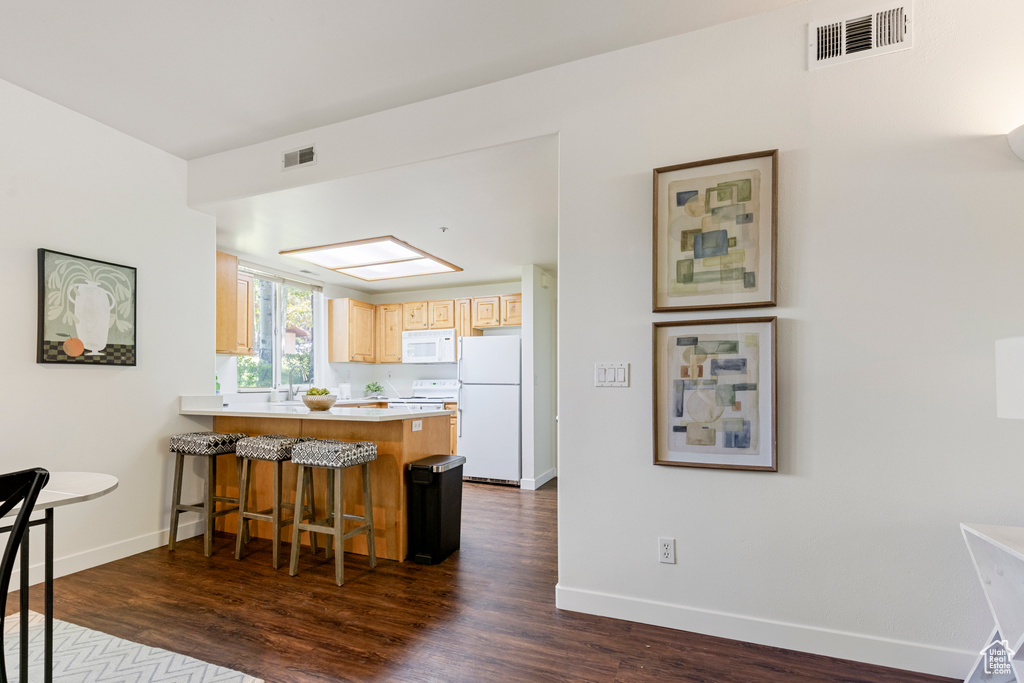 Kitchen featuring white appliances, light brown cabinets, a peninsula, baseboards, and dark wood-style flooring