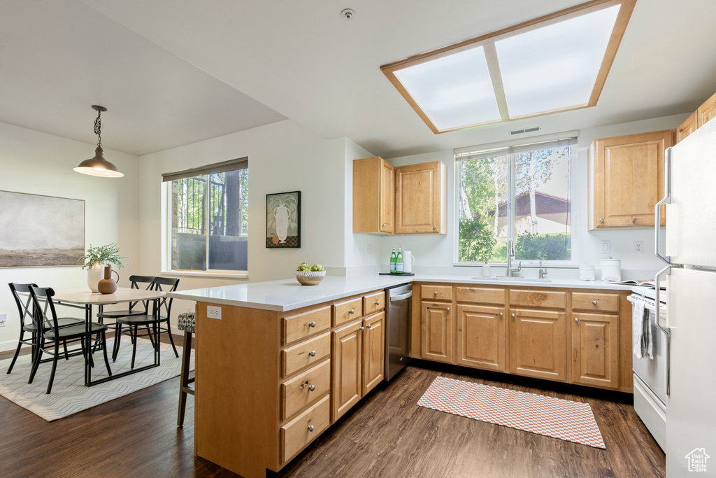 Kitchen featuring a sink, white appliances, dark wood finished floors, a peninsula, and light brown cabinetry