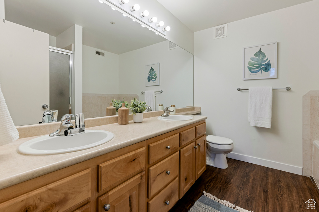 Full bathroom with double vanity, a shower with shower door, wood finished floors, toilet, and baseboards