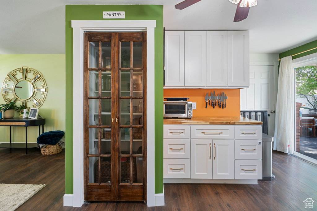 Interior space with white cabinets, a toaster, butcher block counters, dark wood-style flooring, and ceiling fan