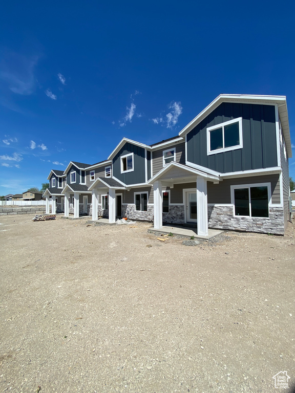 Back of property with stone siding, covered porch, board and batten siding, and fence