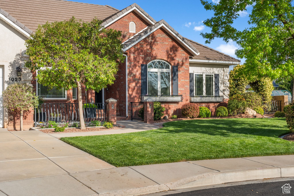 View of front of house with a tiled roof, a fenced front yard, a gate, brick siding, and a front yard