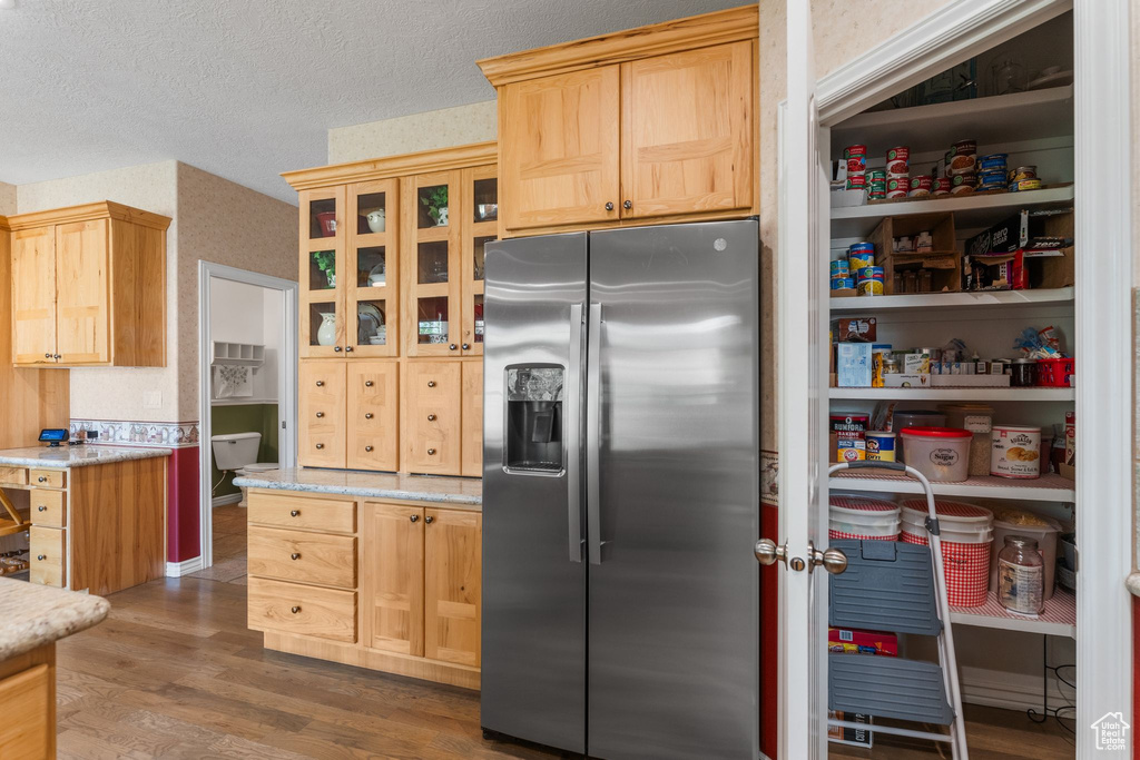 Kitchen with light brown cabinetry, stainless steel fridge with ice dispenser, wood finished floors, glass insert cabinets, and a textured ceiling