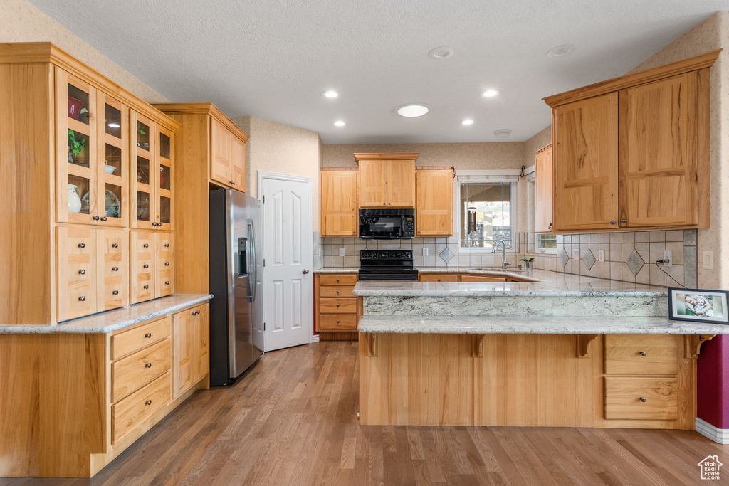 Kitchen featuring tasteful backsplash, black appliances, glass insert cabinets, light wood-type flooring, and a peninsula
