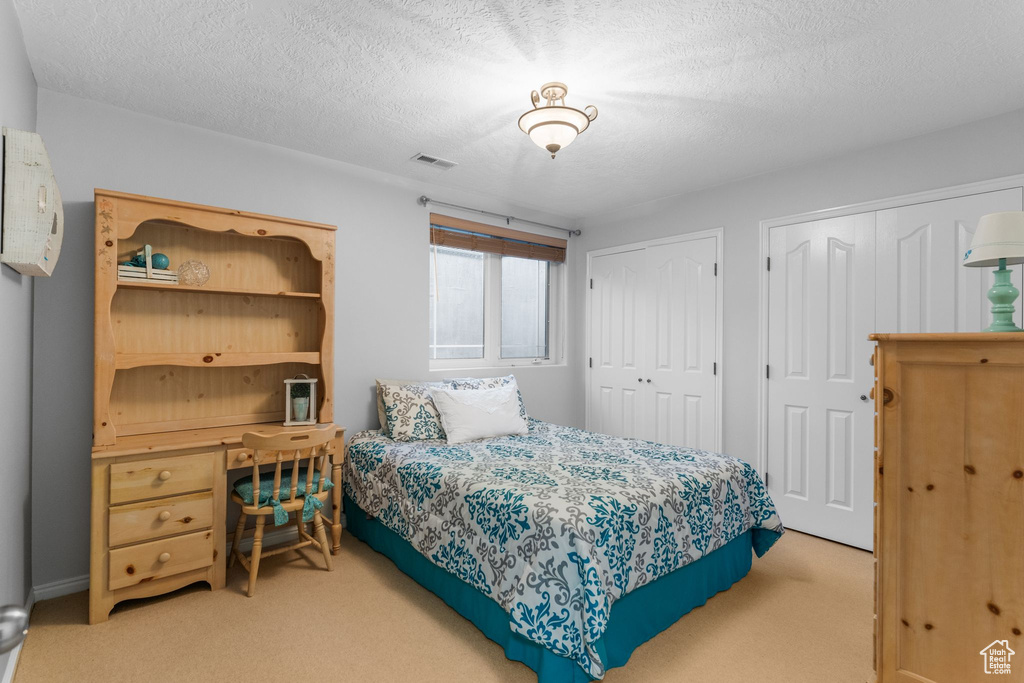 Bedroom with multiple closets, visible vents, a textured ceiling, and light colored carpet