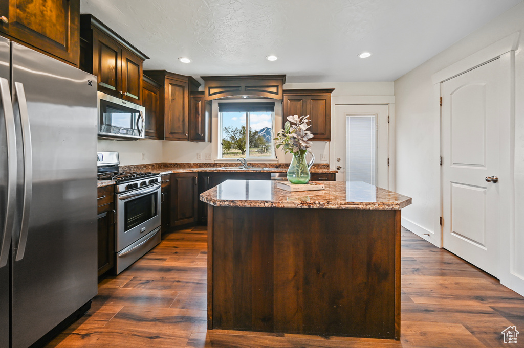 Kitchen with dark brown cabinets, light stone counters, a sink, stainless steel appliances, and a kitchen island