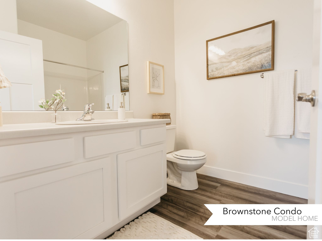 Bathroom with toilet, vanity, wood finished floors, and baseboards