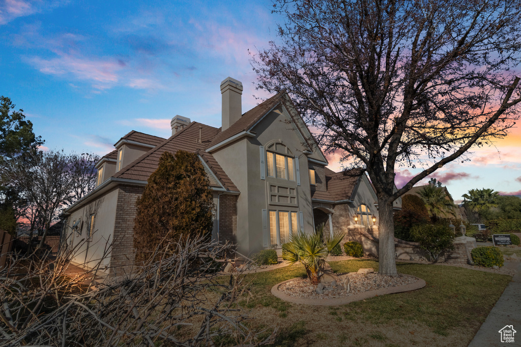 Property exterior at dusk with a chimney, a yard, stucco siding, a tile roof, and brick siding