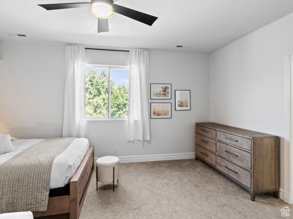 Bedroom featuring visible vents, baseboards, a textured ceiling, light colored carpet, and ceiling fan