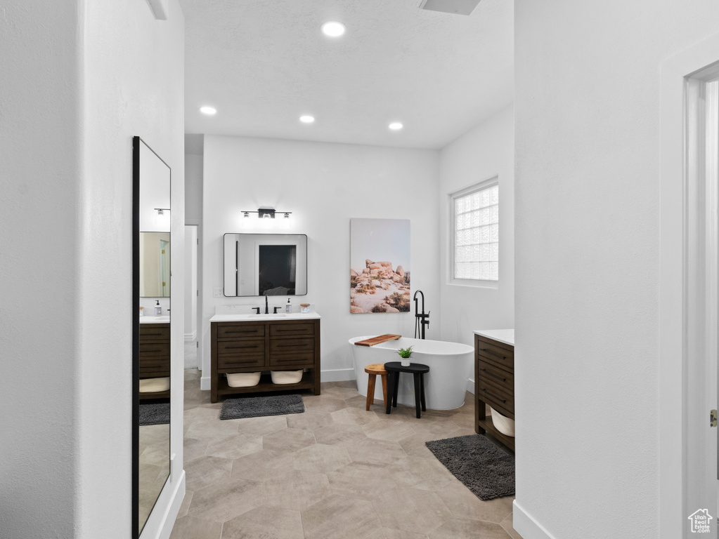 Bathroom featuring a sink, two vanities, a freestanding bath, baseboards, and recessed lighting