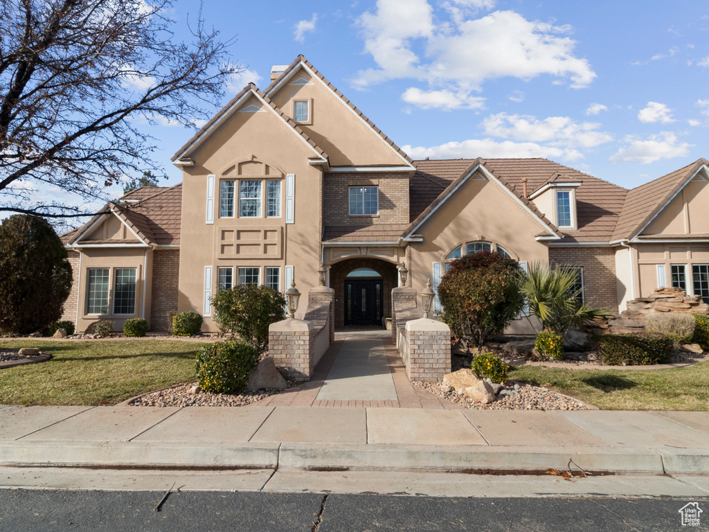 Traditional-style house with a tile roof, a chimney, a front yard, and stucco siding
