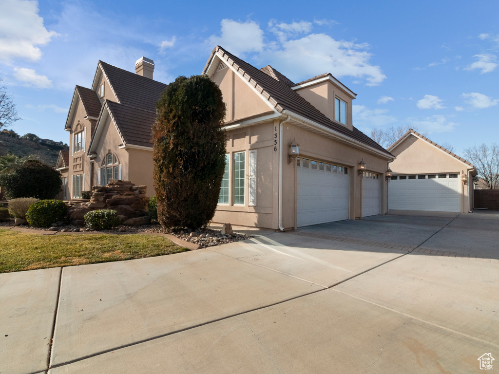 View of property exterior featuring stucco siding, a chimney, concrete driveway, and a tile roof