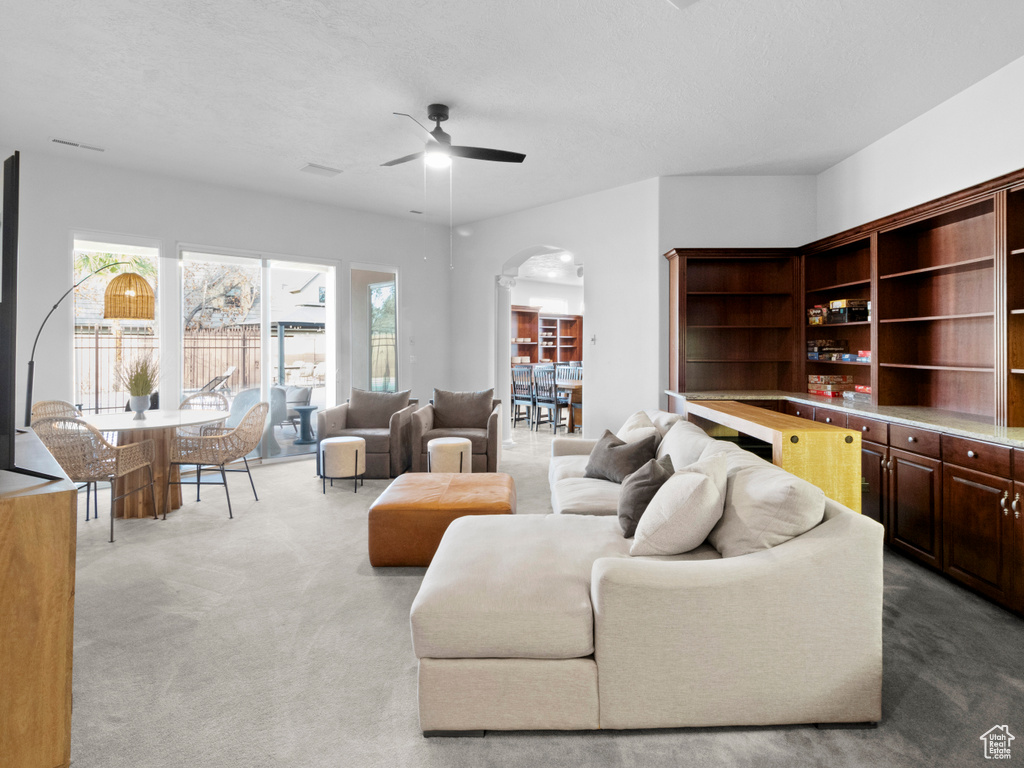 Carpeted living room with arched walkways and ceiling fan