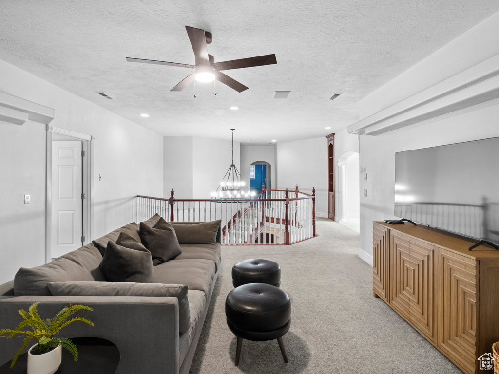 Living room featuring a textured ceiling, ceiling fan with notable chandelier, arched walkways, light colored carpet, and recessed lighting