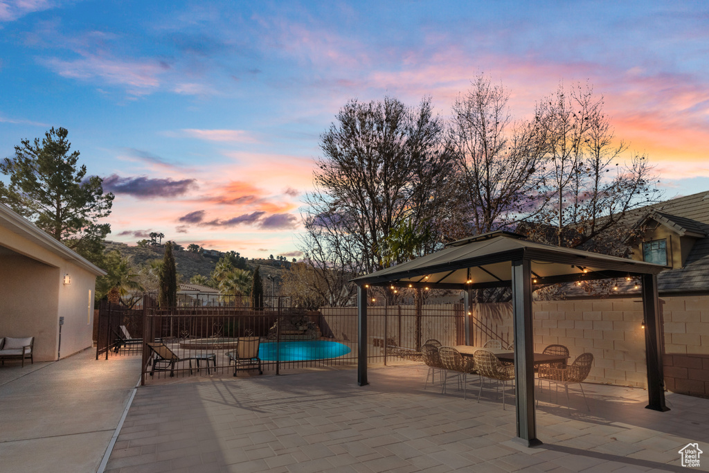 Patio terrace at dusk with a gazebo, a fenced in pool, and fence