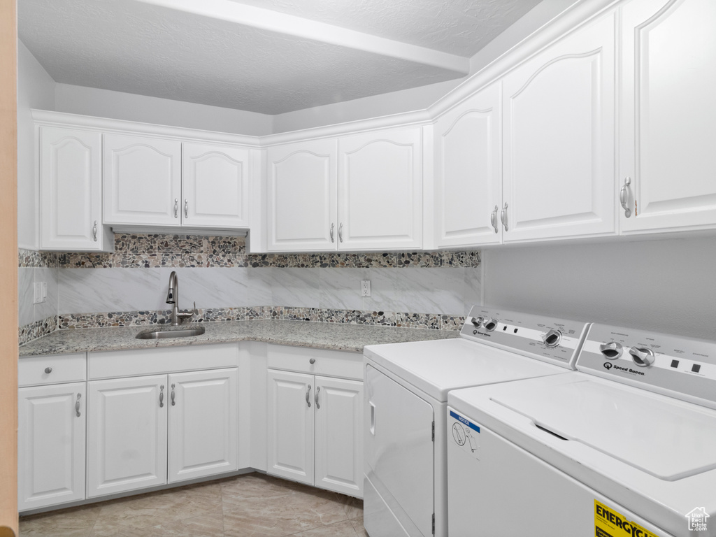 Clothes washing area featuring cabinet space, light tile patterned floors, separate washer and dryer, and a sink
