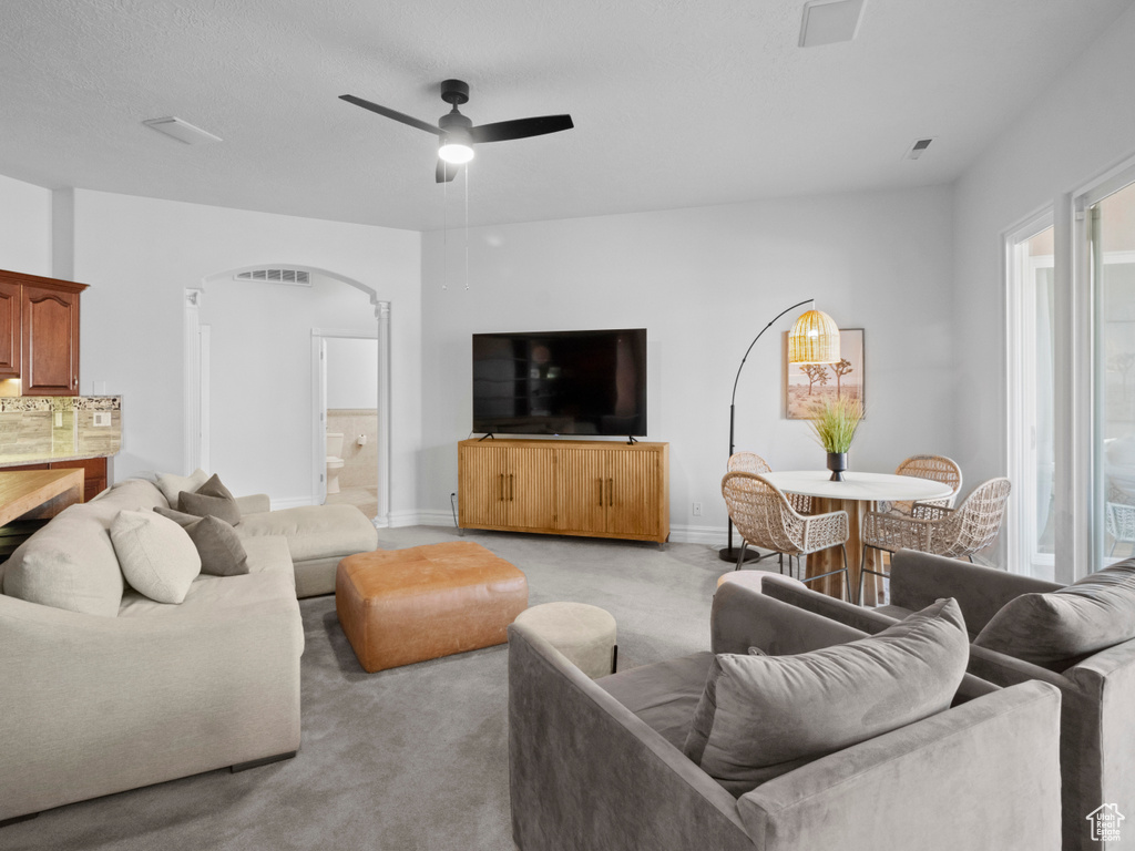 Living area with a ceiling fan, arched walkways, light colored carpet, baseboards, and visible vents