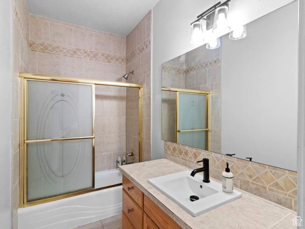 Bathroom with backsplash, combined bath / shower with glass door, and vanity