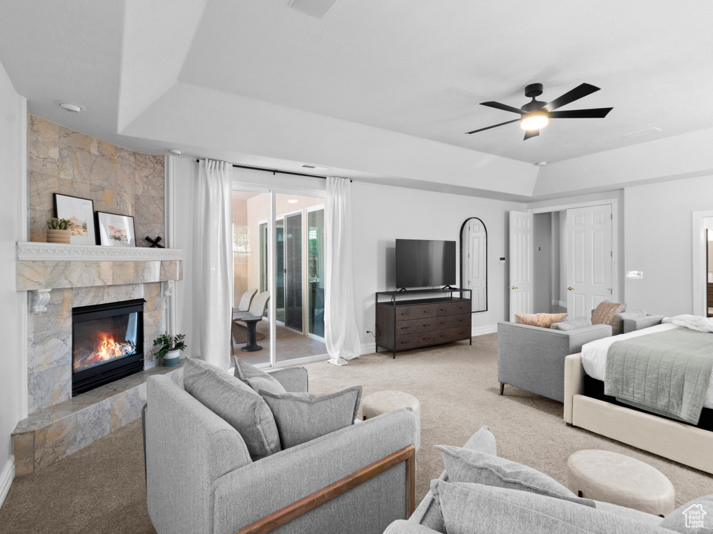Carpeted bedroom with ceiling fan, a raised ceiling, a fireplace, baseboards, and access to exterior