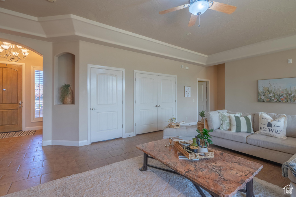 Living room with a ceiling fan, baseboards, arched walkways, and a tray ceiling