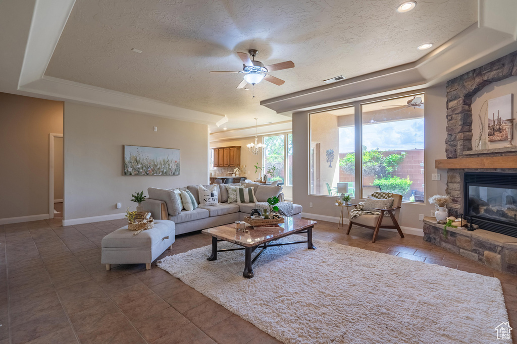 Living area with a textured ceiling, ceiling fan with notable chandelier, a raised ceiling, baseboards, and visible vents