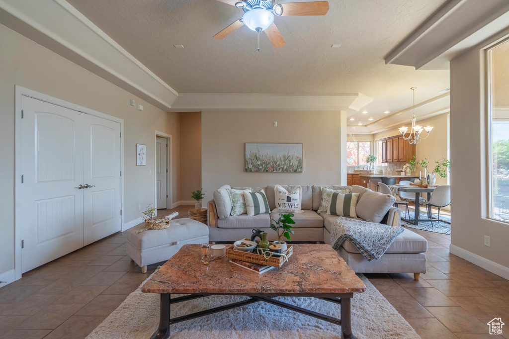 Living area featuring ceiling fan with notable chandelier, baseboards, and light tile patterned floors
