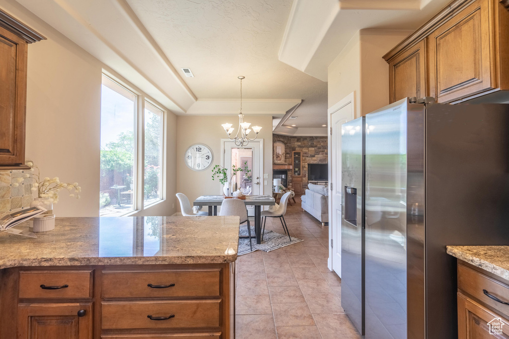 Kitchen featuring brown cabinetry, a chandelier, light tile patterned floors, stainless steel fridge, and decorative light fixtures