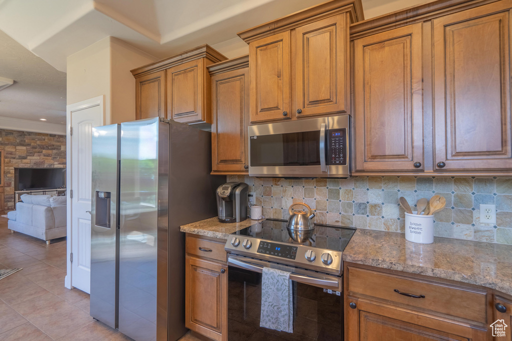 Kitchen featuring stainless steel appliances, decorative backsplash, brown cabinetry, and light stone counters