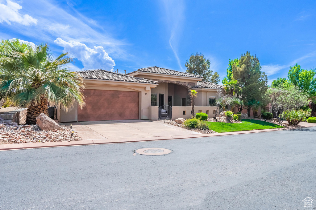 View of front of property featuring an attached garage, a tiled roof, driveway, and stucco siding