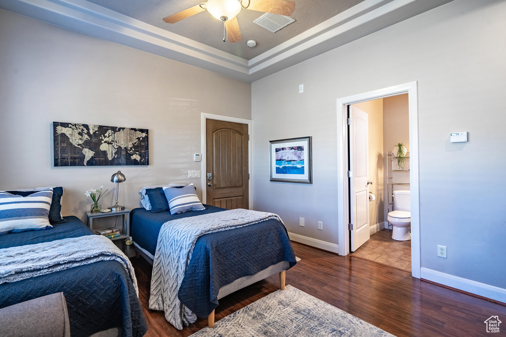 Bedroom featuring a ceiling fan, wood finished floors, baseboards, ensuite bath, and a raised ceiling
