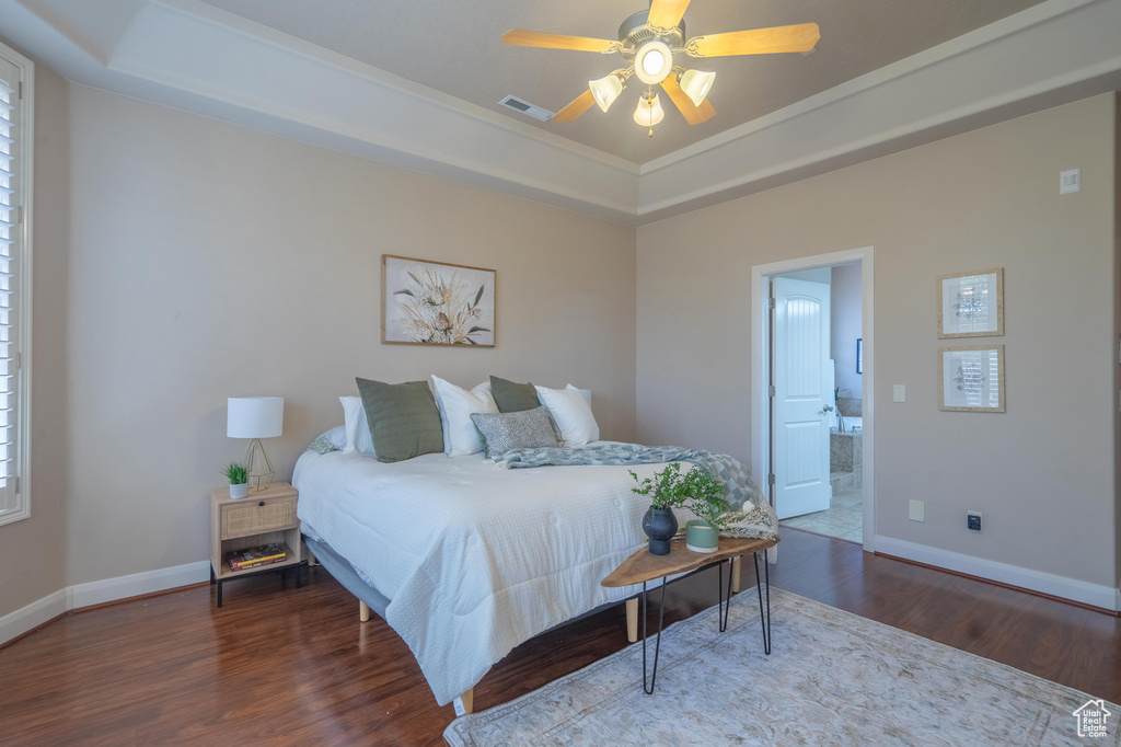Bedroom with a raised ceiling, wood finished floors, visible vents, and baseboards