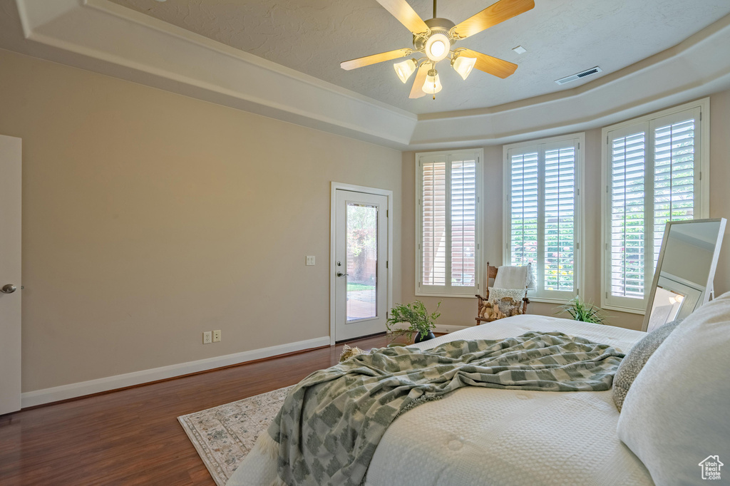 Bedroom with visible vents, baseboards, wood finished floors, access to outside, and a raised ceiling