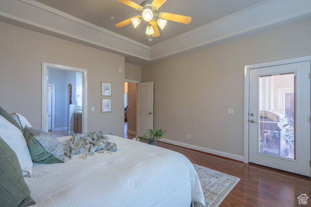 Bedroom featuring a tray ceiling, wood finished floors, connected bathroom, baseboards, and ceiling fan