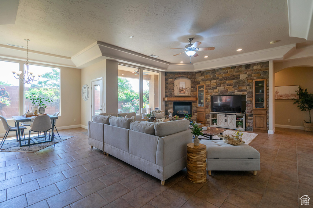 Living area featuring tile patterned floors, a tray ceiling, baseboards, recessed lighting, and ceiling fan with notable chandelier