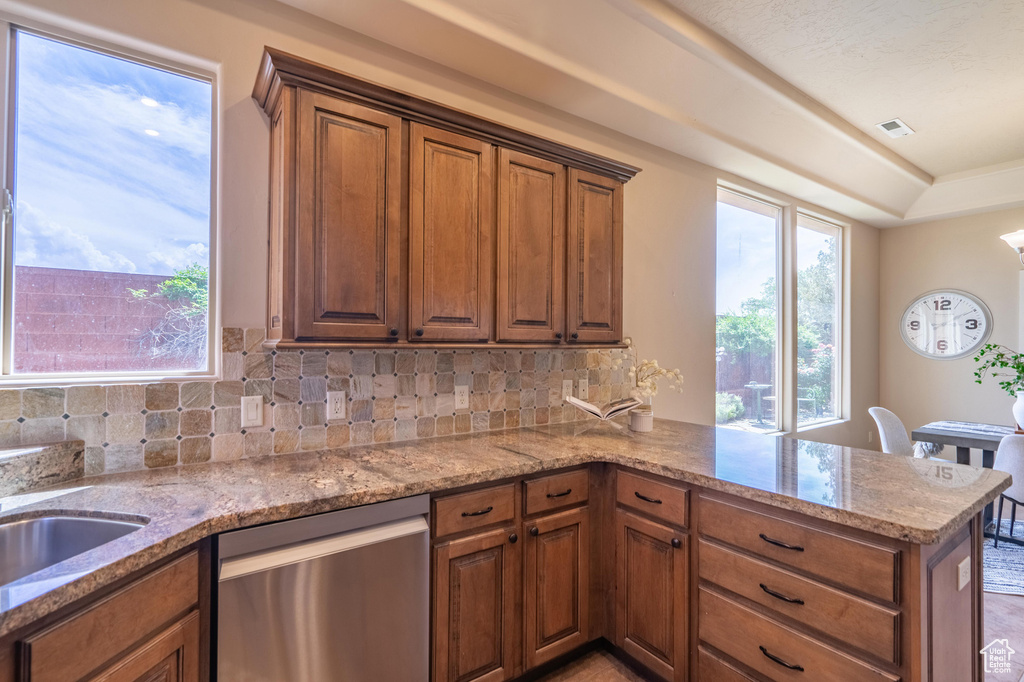 Kitchen with backsplash, a peninsula, stainless steel dishwasher, and brown cabinets