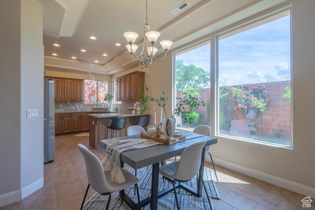 Dining room with light tile patterned floors, an inviting chandelier, a raised ceiling, baseboards, and visible vents