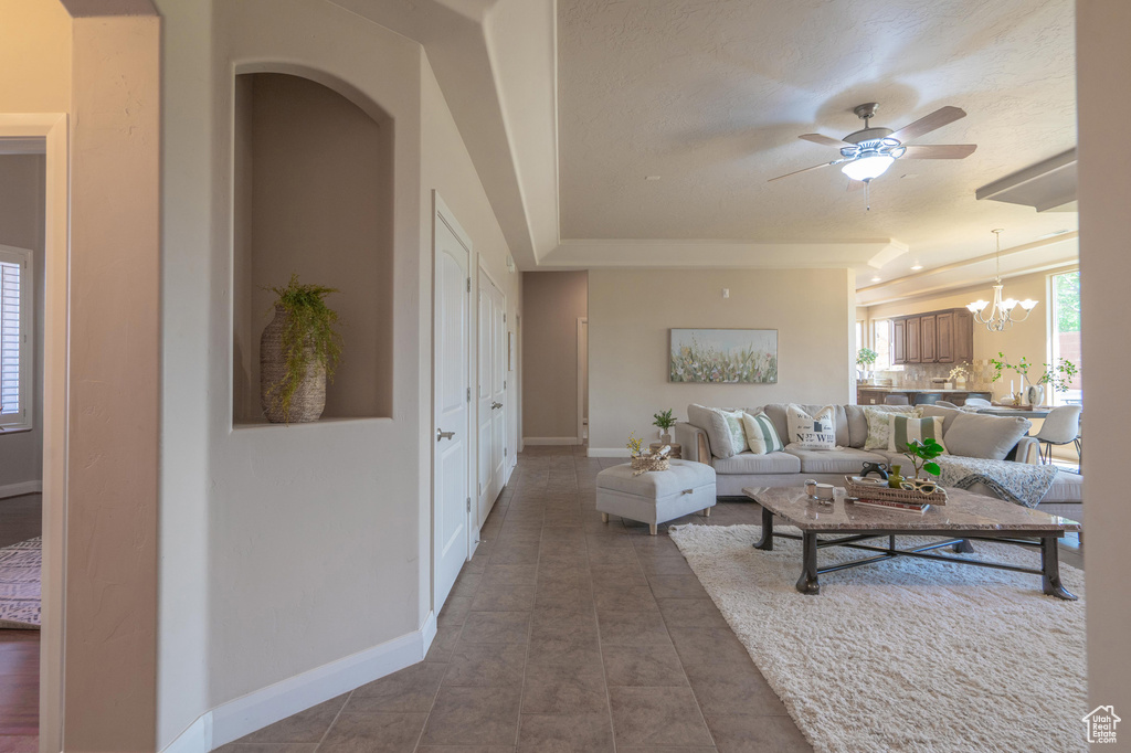 Living room with tile patterned flooring, baseboards, and ceiling fan with notable chandelier