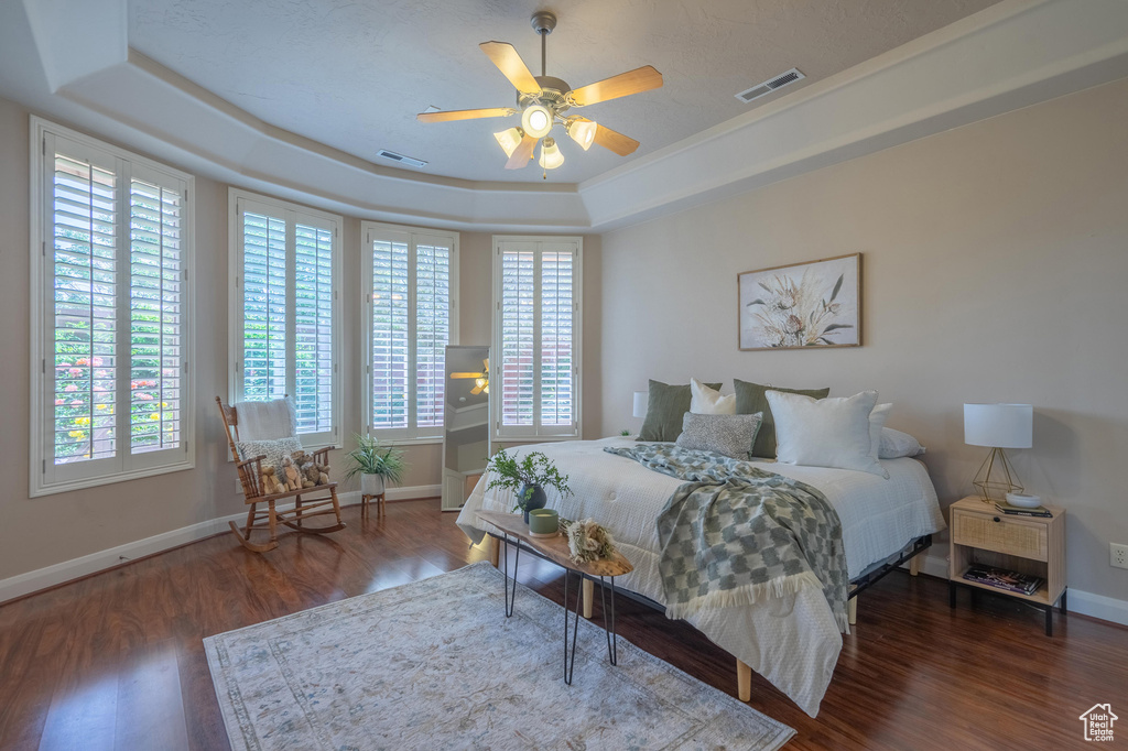 Bedroom featuring a tray ceiling, wood finished floors, visible vents, and baseboards