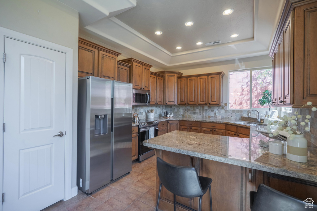 Kitchen featuring stainless steel appliances, a tray ceiling, tasteful backsplash, visible vents, and brown cabinetry