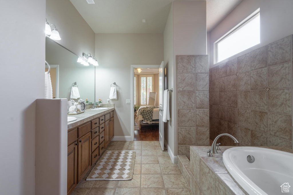 Ensuite bathroom with a sink, a bath, connected bathroom, double vanity, and baseboards