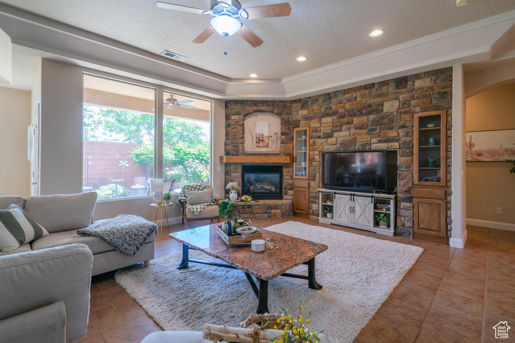 Tiled living room featuring a tray ceiling, visible vents, recessed lighting, ceiling fan, and a stone fireplace