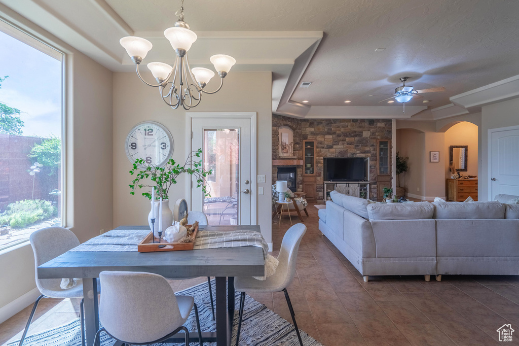 Tiled dining room with arched walkways, baseboards, visible vents, ceiling fan with notable chandelier, and a raised ceiling