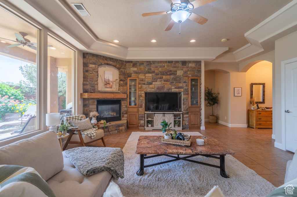 Tiled living room featuring a tray ceiling, visible vents, arched walkways, a fireplace, and ceiling fan