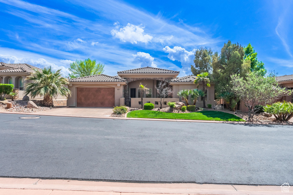 View of front of property featuring stucco siding, a tile roof, concrete driveway, and an attached garage