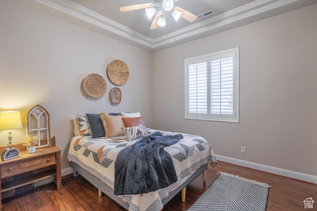Bedroom featuring a tray ceiling, wood finished floors, visible vents, baseboards, and ceiling fan