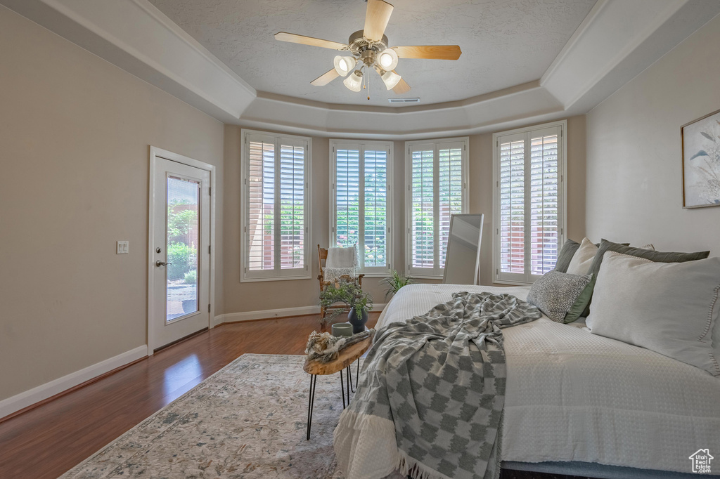 Bedroom featuring a tray ceiling, wood finished floors, access to exterior, a ceiling fan, and baseboards