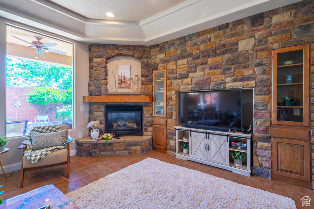Tiled living room featuring a raised ceiling, baseboards, a ceiling fan, and a fireplace