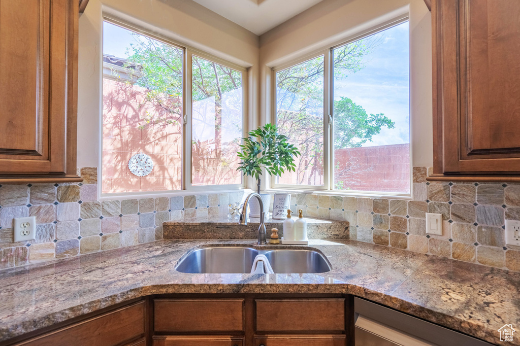 Kitchen with light stone countertops, brown cabinetry, a sink, and backsplash